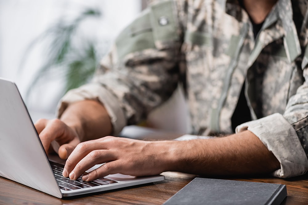 A man in uniform types on a laptop