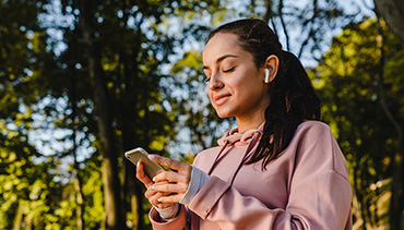 Woman holding phone with earbuds in ears outside