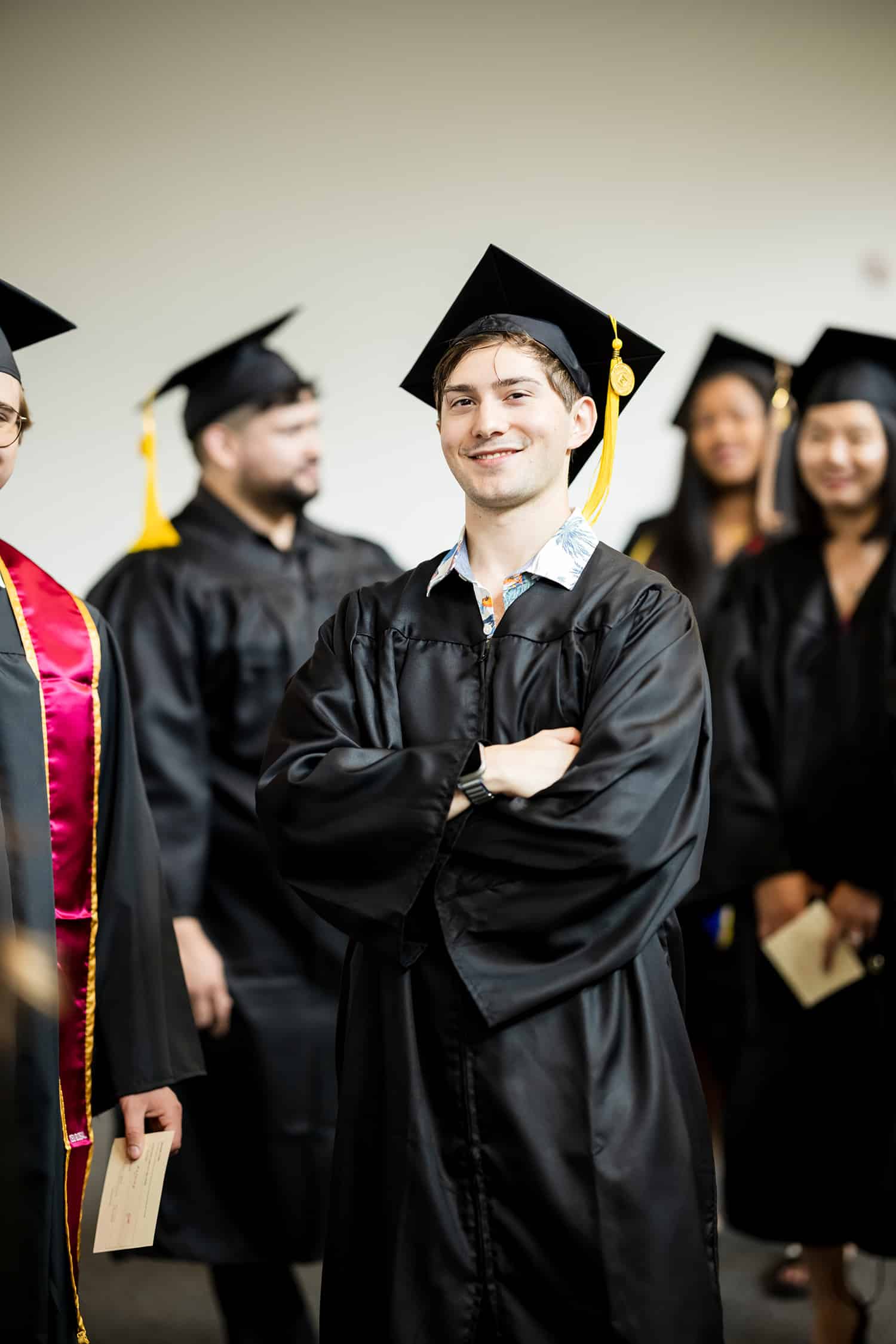 A young man in a cap and gown smiles proudly at the camera